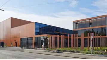 Modernes Geschäftsgebäude mit Glasfassade und braunen Paneelen unter blauem Himmel an einer Straße.