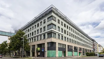 Modernes Büro- und Geschäftsgebäude an einer Straßenecke mit vielen Fenstern und einer markanten Architektur.