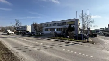 Blick auf das moderne Geschäftsgebäude mit Parkplätzen und Zufahrtsstraße unter blauem Himmel.