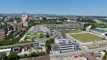 Luftaufnahme eines Gewerbegebiets mit modernen Gebäuden, Solaranlagen und städtischer Umgebung.