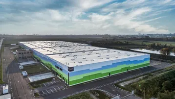 Drohnenaufnahme eines großen, modernen Logistikzentrums mit farbiger Fassade und weitläufigen Parkplätzen.