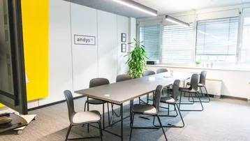 Moderner Konferenzraum mit großem Tisch, bequemen Stühlen und viel Tageslicht durch große Fenster.