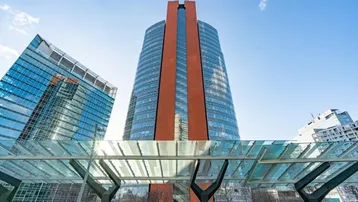 Moderne Hochhäuser mit Glasfassaden und einem markanten roten Turm unter blauem Himmel.