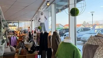 Heller Verkaufsraum mit großen Schaufenstern, Kleidung auf Schaufensterpuppen und Blick auf die Straße.