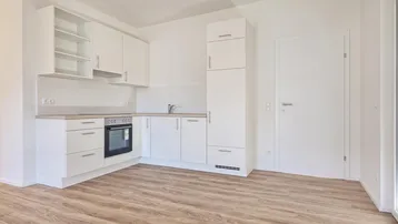 Helle, unmöblierte Küche mit weißen Schränken, Backofen und Laminatboden.