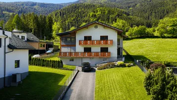 Modernes Wohnhaus mit mehreren Balkonen und gepflegtem Garten in alpiner Umgebung.