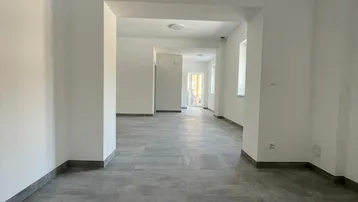 Langer, heller Raum mit modernen grauen Fliesen und weißen Wänden, der sich durch mehrere Öffnungen erstreckt.