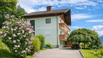 Wohnhaus mit hellgrüner Fassade, Holzbalkonen und gepflasterter Auffahrt.