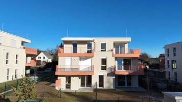 Modernes Mehrfamilienhaus mit hellen Fassaden und orangefarbenen Balkonen unter blauem Himmel.