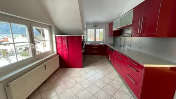Geräumige Küche mit leuchtend roten Hochglanzschränken, Fliesenboden und Blick auf die Umgebung.