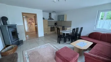 Gemütlicher offener Wohn-Essbereich mit integrierter Küche, Kaminofen und Fliesenboden.