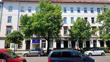 Klassisches Wiener Wohngebäude mit Bäumen und parkenden Autos auf der Straße.