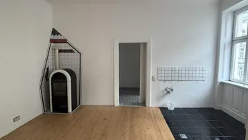 Heller Raum mit Holzdielen, Fliesenbereich und einem modernen Holzofen.