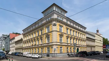 Historisches Gebäude mit gelber Fassade und moderner Dachaufstockung an einer Straßenecke.