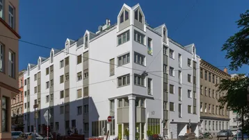 Modernes Wohngebäude mit weißer Fassade, vielen Fenstern und markanten Dachgauben an einer Straßenecke.
