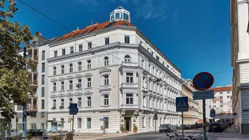 Elegantes Eckgebäude in urbaner Umgebung mit klassischer Architektur und vielen Fenstern.