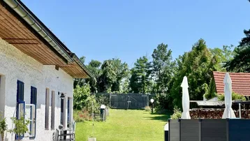 Langer Gartenbereich neben dem Haus mit Rasenfläche und einem kleinen Sitzbereich im Freien.