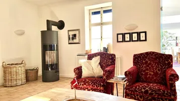 Gemütliches Wohnzimmer mit Terrakottaboden, Kaminofen und zwei roten Polstersesseln.