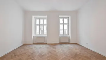 Helles Zimmer mit Fischgrätparkettboden und zwei Fenstern, bereit zur individuellen Gestaltung.