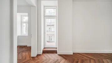 Helles Zimmer mit Fischgrätparkett und einem französischen Balkon mit Blick auf die Straße.
