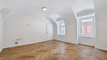 Helles Zimmer mit Fischgrätparkett, gewölbten Decken und zwei Fenstern, bereit für die Einrichtung.