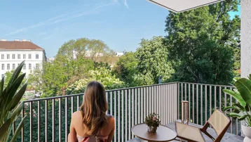 Eine Person genießt den Ausblick von einem modernen Balkon mit Blick ins Grüne und auf die Stadt.