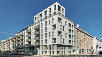 Modernes Eckgebäude mit mehreren Etagen und Balkonen an einer städtischen Kreuzung.