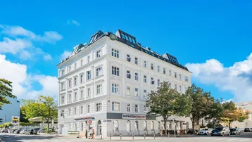 Eindrucksvolles Eckgebäude mit klassischer Architektur und hellen Fassaden unter blauem Himmel.