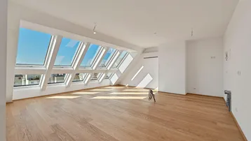 Helles Dachgeschosszimmer mit Holzboden und großen Dachfenstern, das viel Tageslicht hereinlässt.