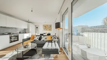 Helles, offenes Wohnzimmer mit integrierter Küche, modernem Sofa und direktem Zugang zum sonnigen Balkon.