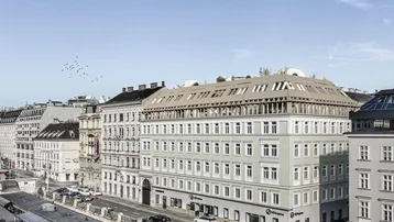 Luftaufnahme eines modernen Stadtgebäudes mit Geschäften im Erdgeschoss und umliegender Stadtlandschaft.