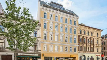 Historisches Gebäude mit modernem Dachausbau und Geschäften im Erdgeschoss an einer Stadtstraße.