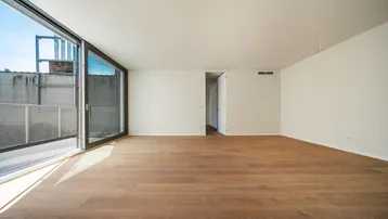 Helles, leeres Zimmer mit Holzboden und großer Schiebetür zu einem Außenbereich.