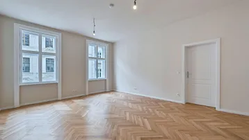Helles Zimmer mit Fischgrätparkett und hohen Fenstern, bereit zur individuellen Gestaltung.
