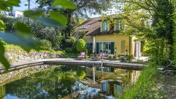 Idyllisches Haus mit Naturpool und Liegefläche, umgeben von üppigem Grün und Bäumen.