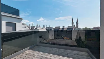 Dachterrasse mit Holzboden, Glasgeländer und Blick auf die Stadt mit Kirchtürmen.