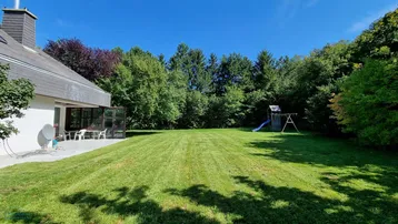 Großer, gepflegter Garten mit Rasenfläche, Spielplatz und einer Terrasse am Haus.