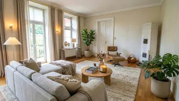 Helles Wohnzimmer mit beigem Sofa, Holzboden und einem traditionellen Kachelofen.