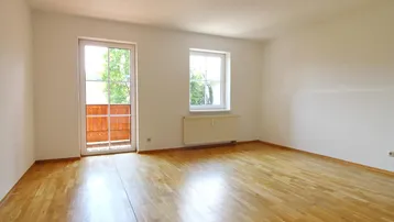 Helles Zimmer mit Parkettboden und Zugang zu einem kleinen Balkon, ideal als Wohn- oder Schlafzimmer.