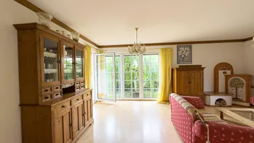 Geräumiges Wohnzimmer mit traditionellen Möbeln, hellem Boden und einem Kachelofen.