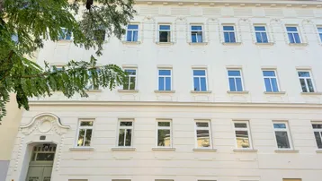 Klassische Fassade eines gepflegten Mehrfamilienhauses mit vielen Fenstern und dekorativen Elementen.