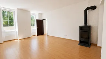 Geräumiges Wohnzimmer mit Laminatboden und einem modernen Holzofen als Wärmequelle.