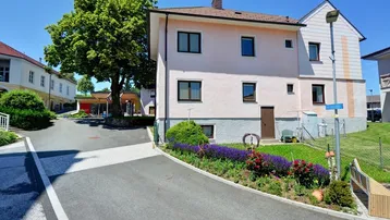 Rosa verputztes Haus mit Satteldach und gepflegtem Vorgarten an einer ruhigen Straße.
