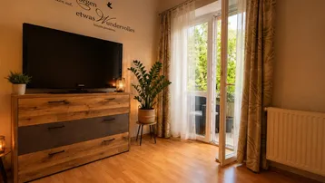 Helles Wohnzimmer mit Holzboden, TV-Möbel und direktem Zugang zu einem Balkon.