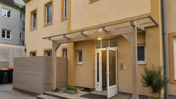 Eingangsbereich eines Mehrfamilienhauses mit Vordach und kleiner Bepflanzung.