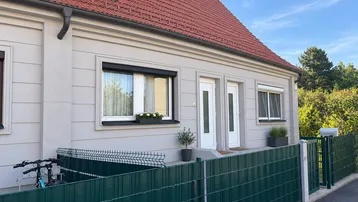 Moderne Doppelhaushälfte mit heller Fassade, roten Dachziegeln und kleinen Vorgärten.