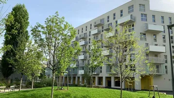 Modernes Wohngebäude mit vielen Balkonen und einer gepflegten Grünfläche im Vordergrund.