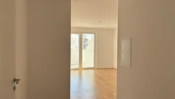 Heller Flur mit Parkettboden, der in einen lichtdurchfluteten Wohnbereich mit Balkonzugang führt.