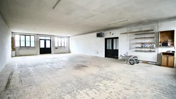 Großer, leerer Gewerberaum mit abgenutztem Holzboden, hohen Decken und mehreren Fenstern, bereit zur Renovierung.