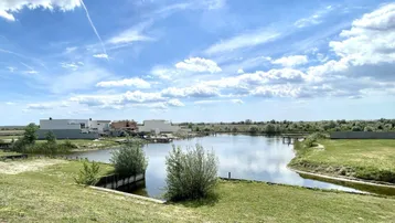 Weitläufige Seenlandschaft mit modernen Häusern am Ufer unter blauem Himmel.
